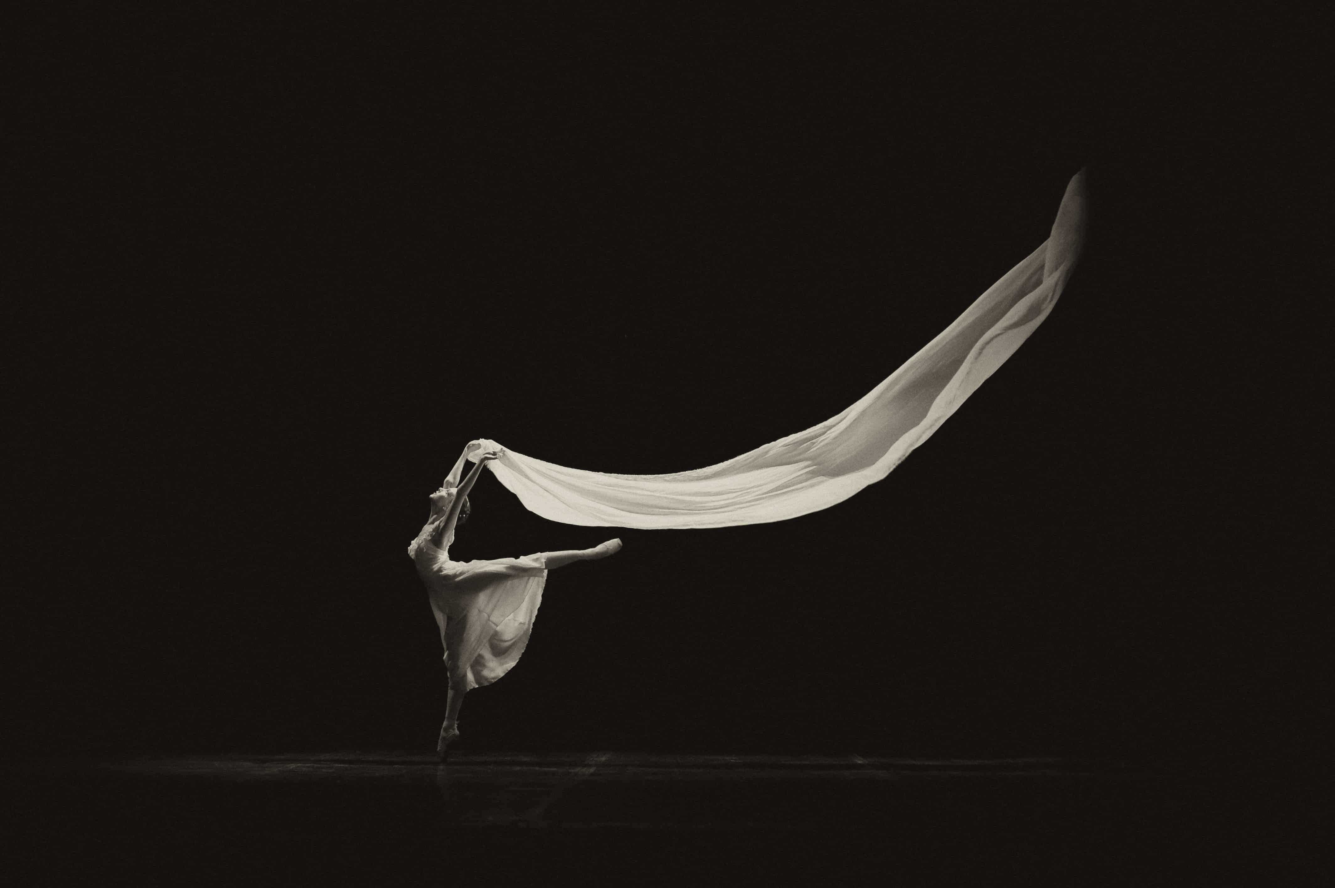 Black and white photo of ballet dancer en pointe holding beautiful flowing fabric behind her.